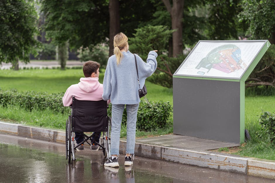A young couple examines a park map, with one partner in a wheelchair, on a rainy day.