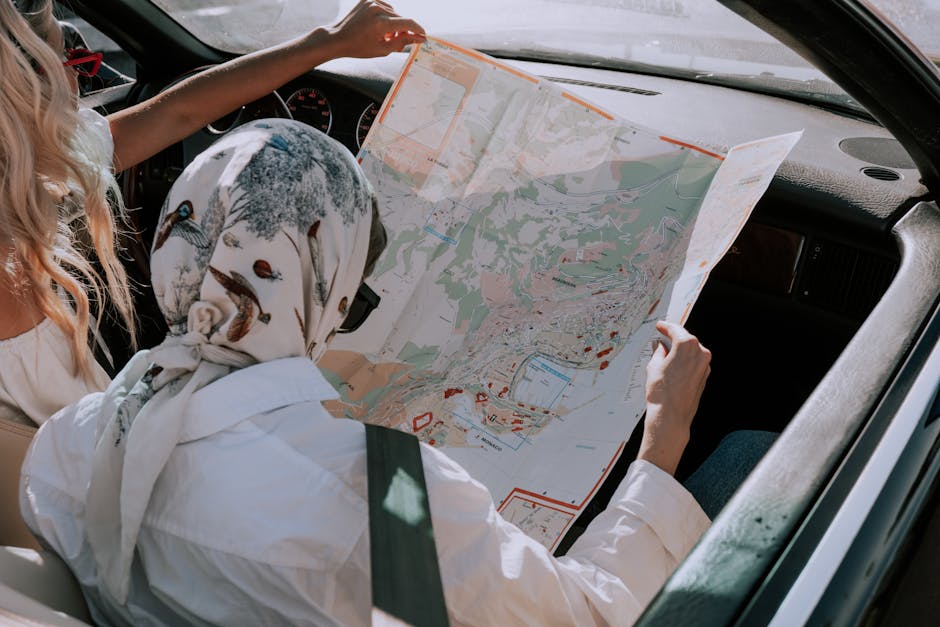 Two friends in a car navigating their road trip using a map during daytime.