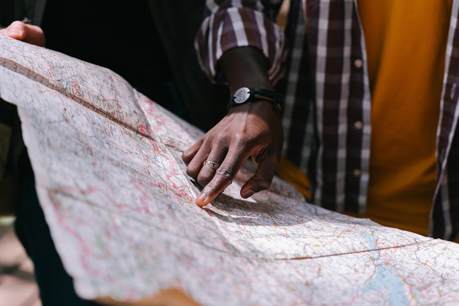 Close-up of a hand pointing at a detailed map, outdoors, wearing a striped shirt.